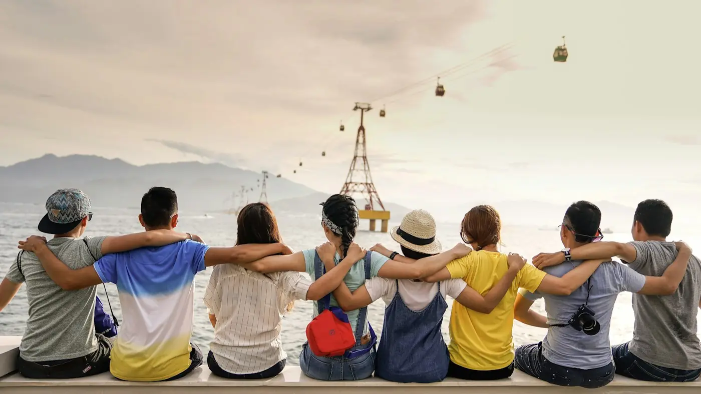 Grupo de jóvenes sentados juntos abrazados mirando hacia el horizonte