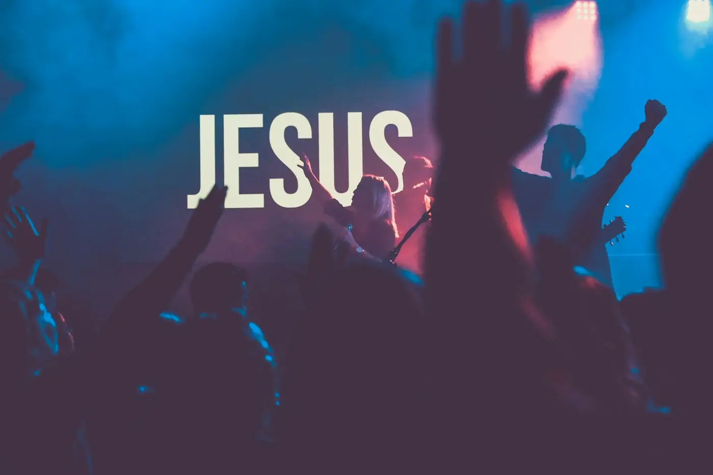 Jóvenes adorando frente a un letrero luminoso que dice JESUS